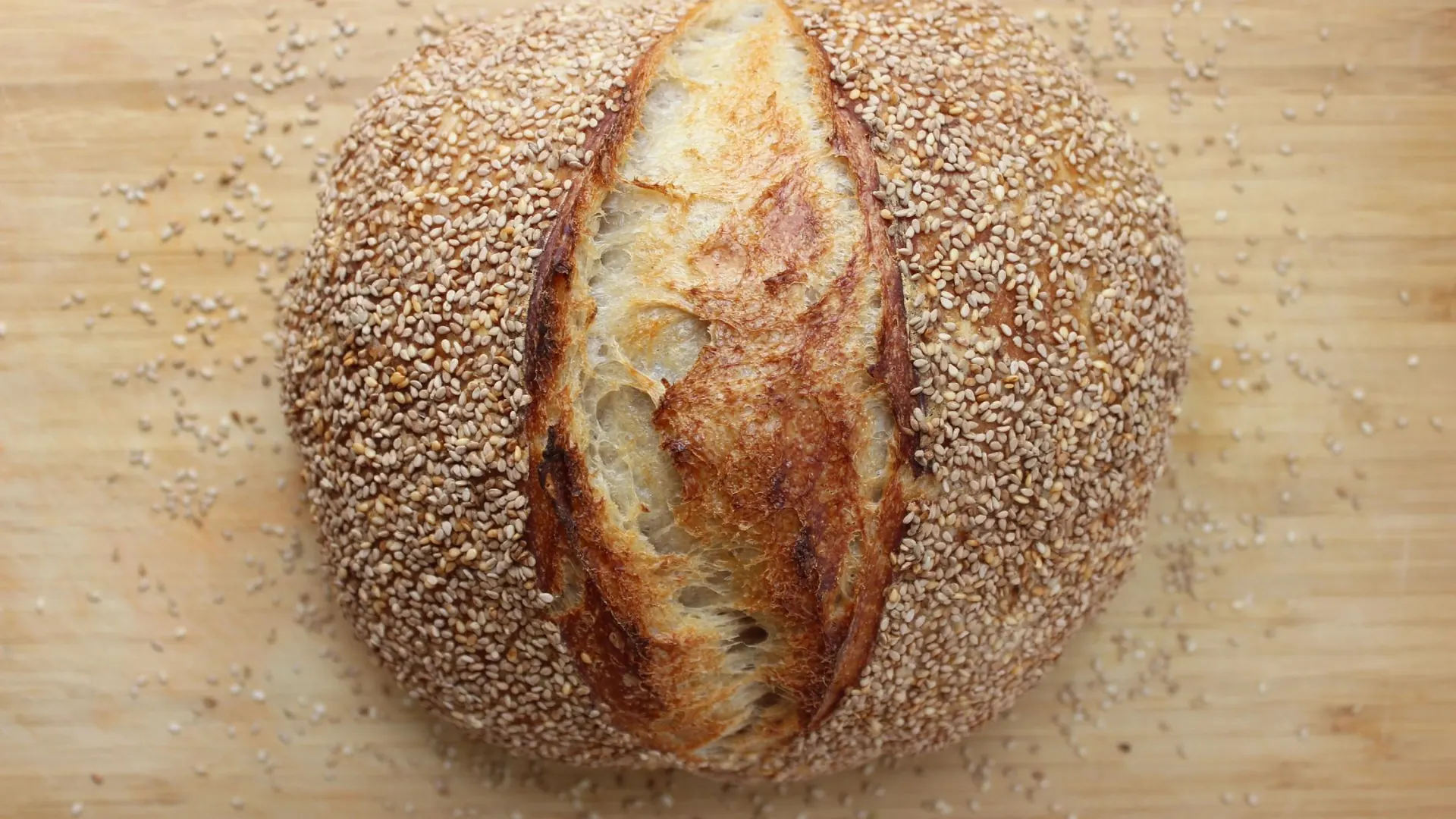 A freshly baked sesame-crusted sourdough loaf on a wooden board
